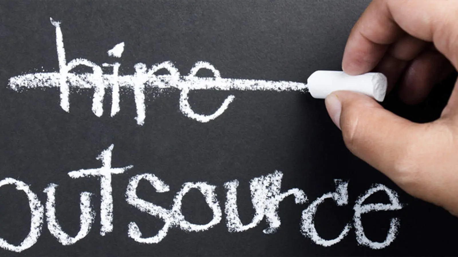 Hand erasing the word "Hire" and replacing it with "Outsource" written in white chalk on a blackboard, highlighting business strategy concepts.