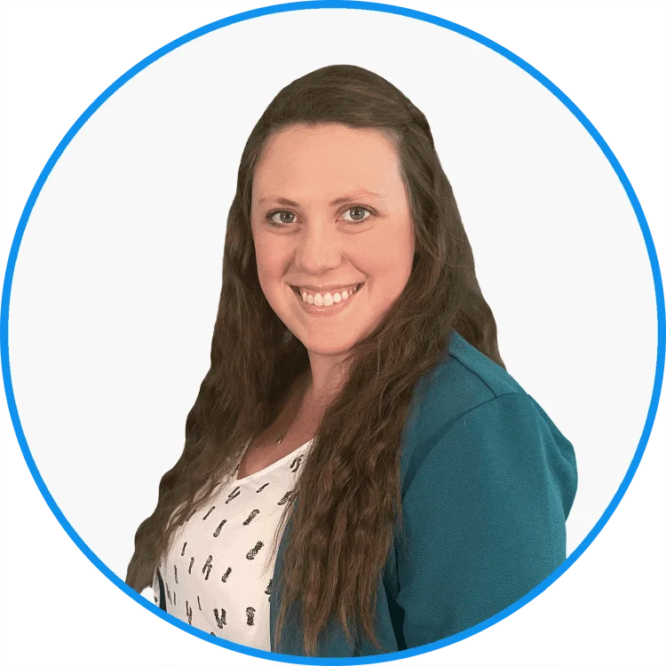 Portrait of a smiling woman with long brown hair, wearing a teal cardigan and a printed white blouse, set against a plain background.