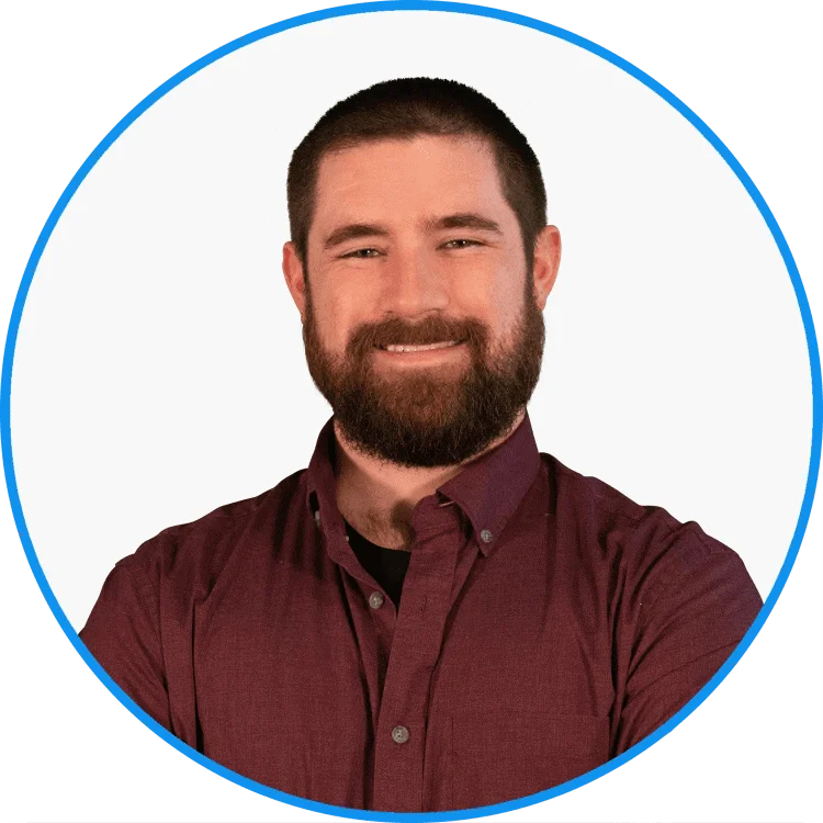 Professional headshot of a smiling bearded man in a dark burgundy shirt, framed by a circular blue border, displaying confidence and approachability.