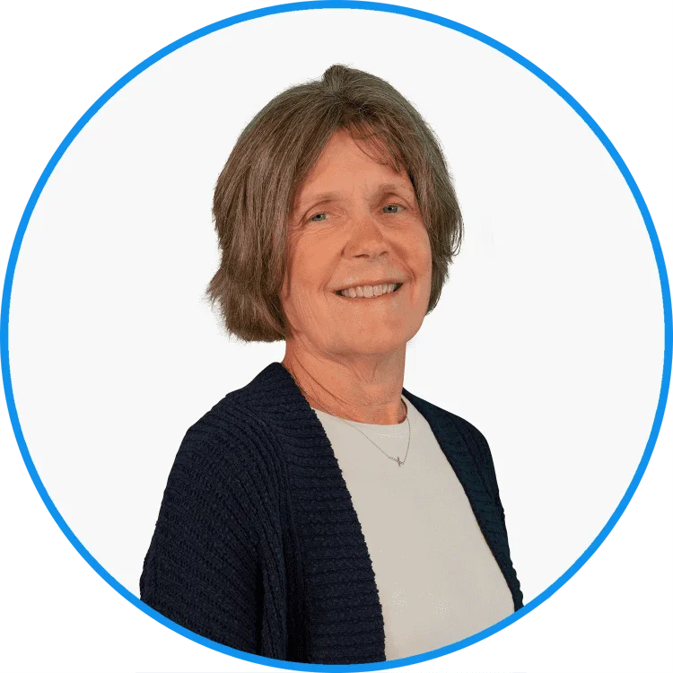 Elderly Caucasian woman smiling warmly, wearing a navy blue cardigan and white shirt, against a white background with blue circle frame.