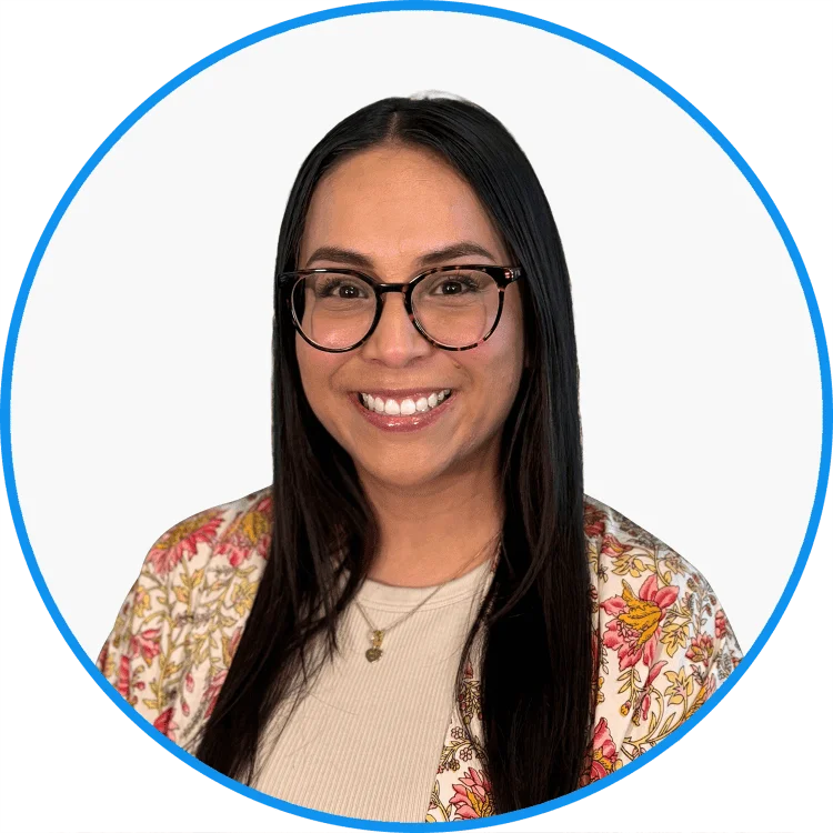 Professional smiling woman with long hair wearing glasses and a floral blazer over a white top, with a blue circular background.