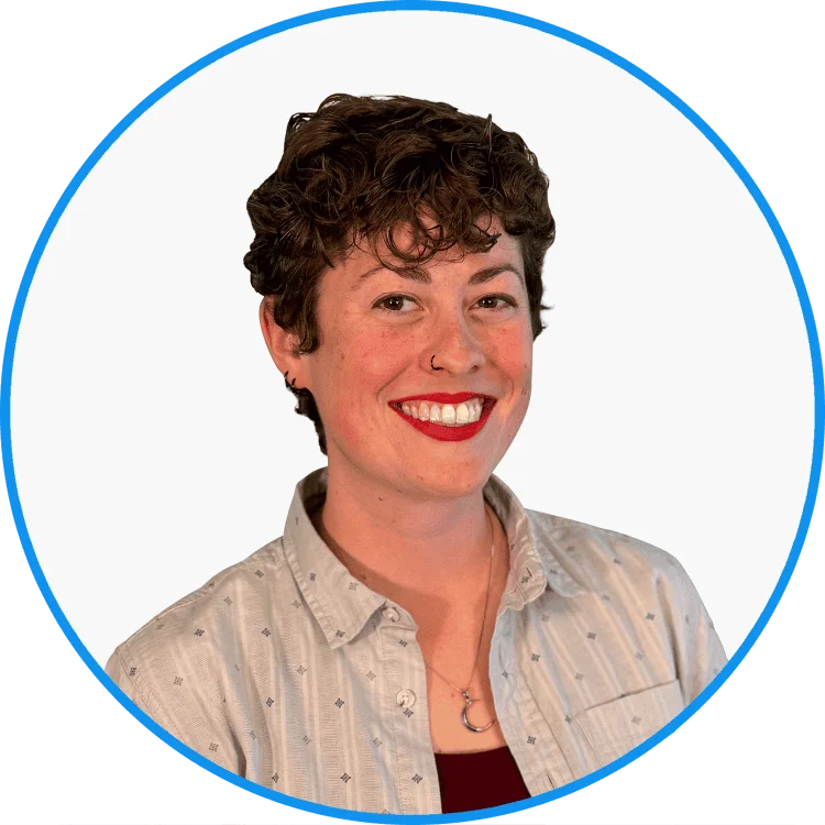 Smiling woman with short curly hair, red lipstick, wearing a light patterned shirt, circular blue bordered portrait.