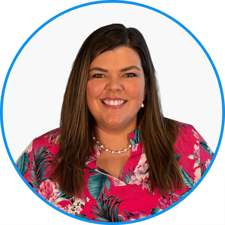 Smiling woman with brunette hair wearing a floral pink blouse and pearl necklace, isolated on a white background with blue circular frame.